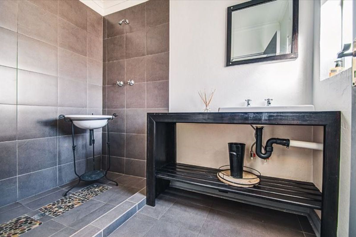 A bathroom featuring dark tiled walls and flooring, a pedestal sink, and a vanity unit with exposed plumbing.