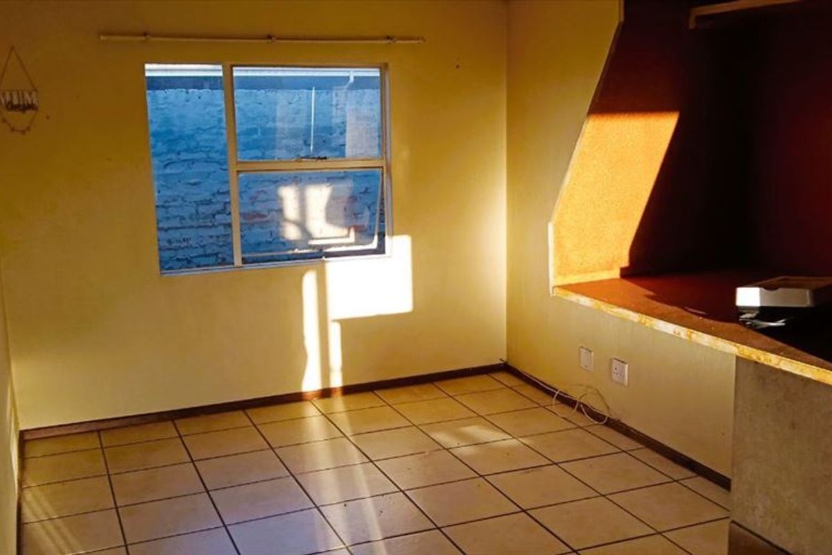 An empty open-plan living area featuring tiled flooring and a built-in counter, offering a blank canvas for potential renovation and interior design updates.