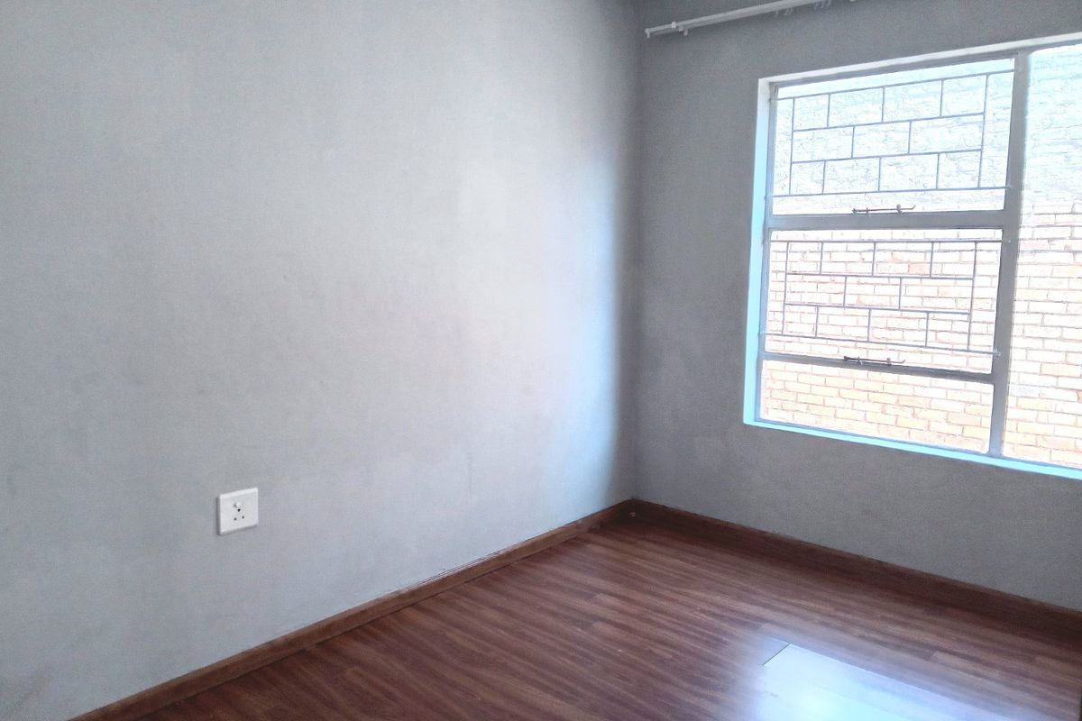An empty bedroom featuring laminate flooring, neutral grey walls, and a window fitted with security bars.