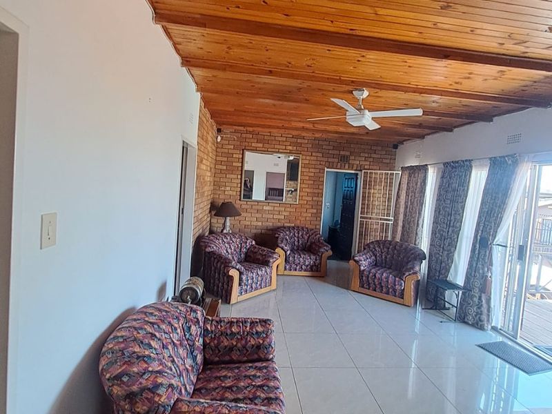 Spacious living area featuring an exposed timber ceiling, exposed brick feature wall, tiled flooring, and large sliding glass doors leading to the exterior.