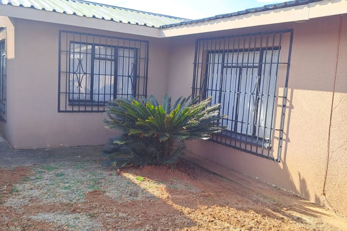 Rear exterior view of the house featuring stucco walls, metal security bars on windows, and a corrugated metal roof.