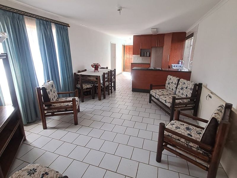 An open-plan living and dining area featuring tiled flooring and a functional kitchen with built-in cabinetry and counter space.