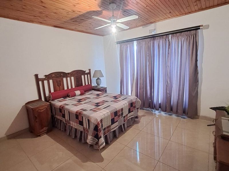 Spacious bedroom featuring polished tiled flooring, a warm timber tongue and groove ceiling, and a central ceiling fan.