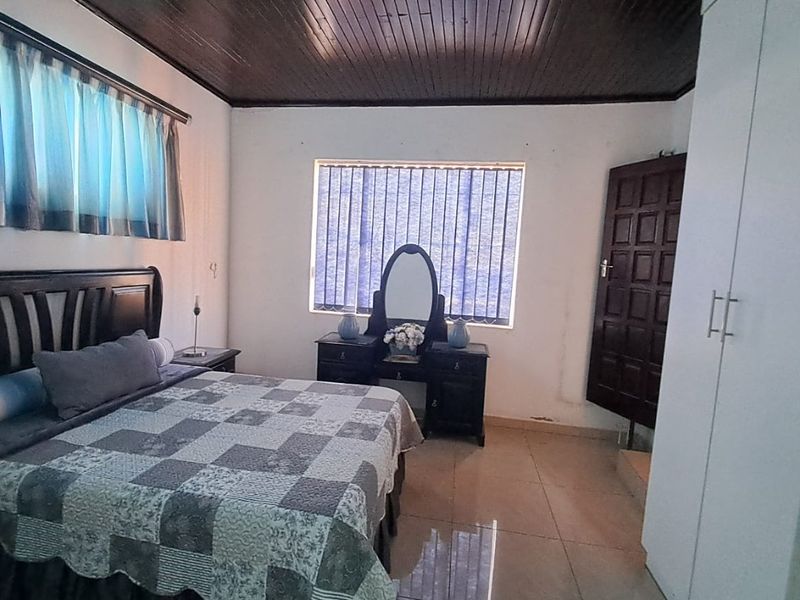 A bedroom featuring tiled flooring, a dark timber ceiling, and a built-in wardrobe, offering a functional space with potential for cosmetic updates.