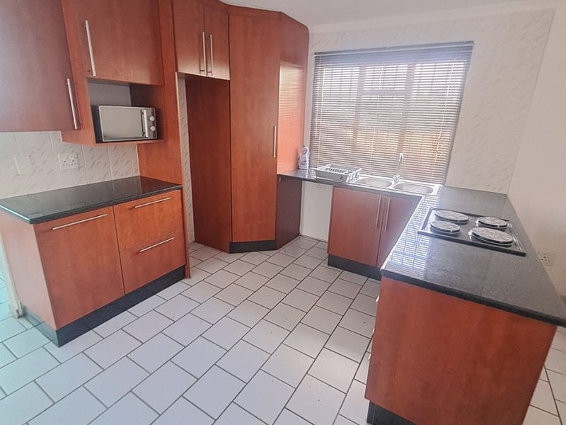 A functional kitchen featuring wooden cabinetry, granite countertops, an integrated electric hob, and a double sink with tiled flooring.