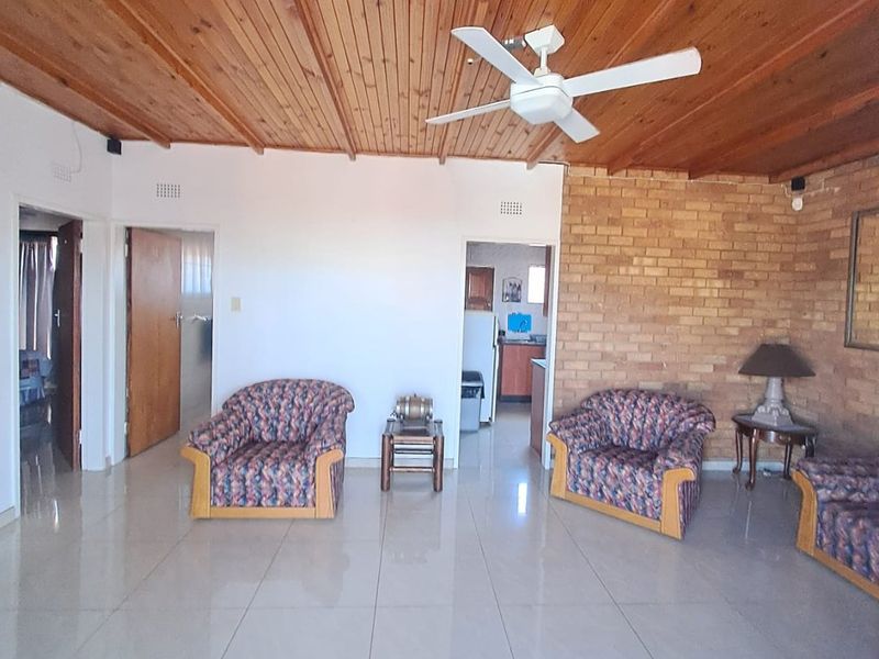 Spacious living area featuring a warm timber-clad ceiling, exposed brick feature wall, and neutral tiled flooring throughout.