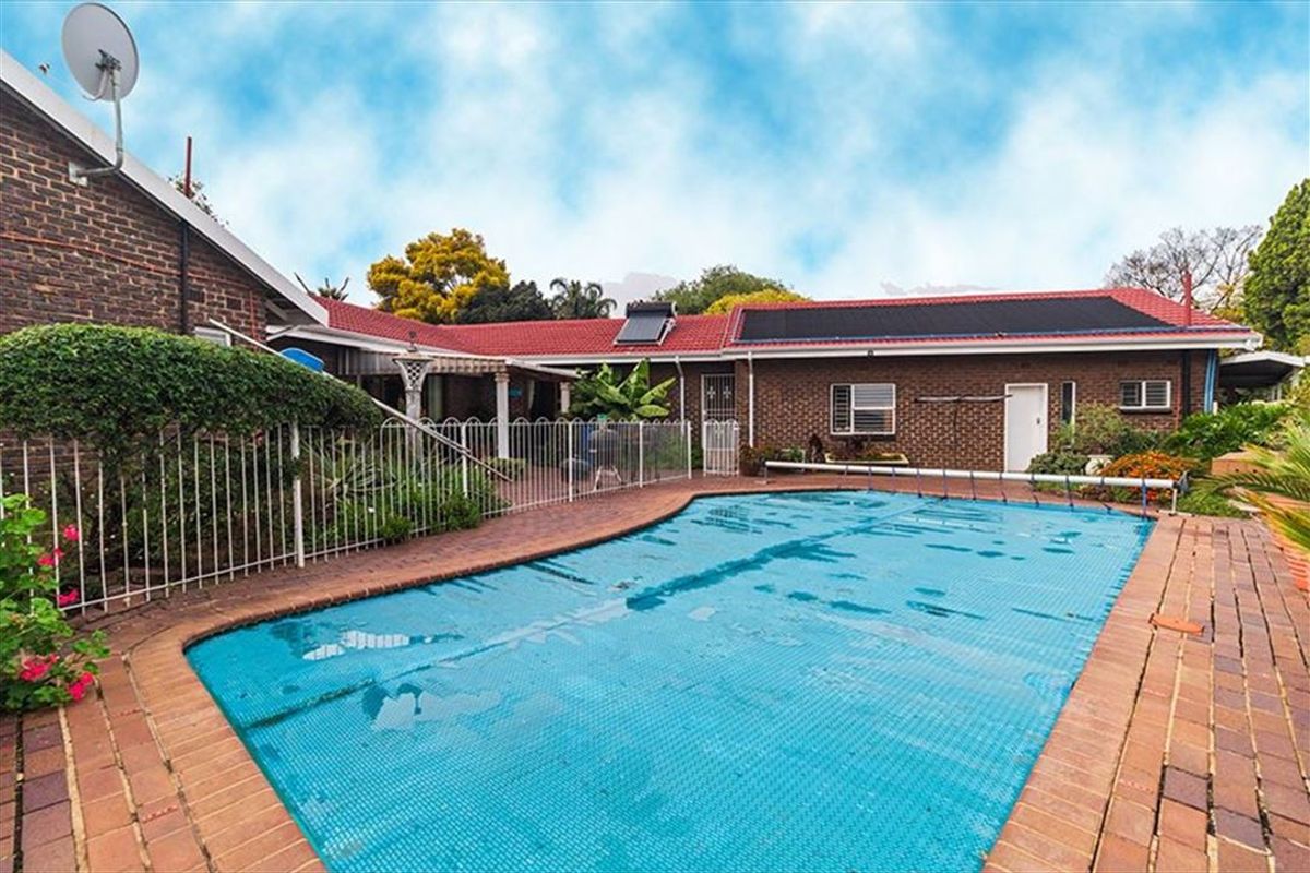 Outdoor pool area featuring a swimming pool with a cover, surrounded by brick paving and enclosed by metal security fencing against a brick house.
