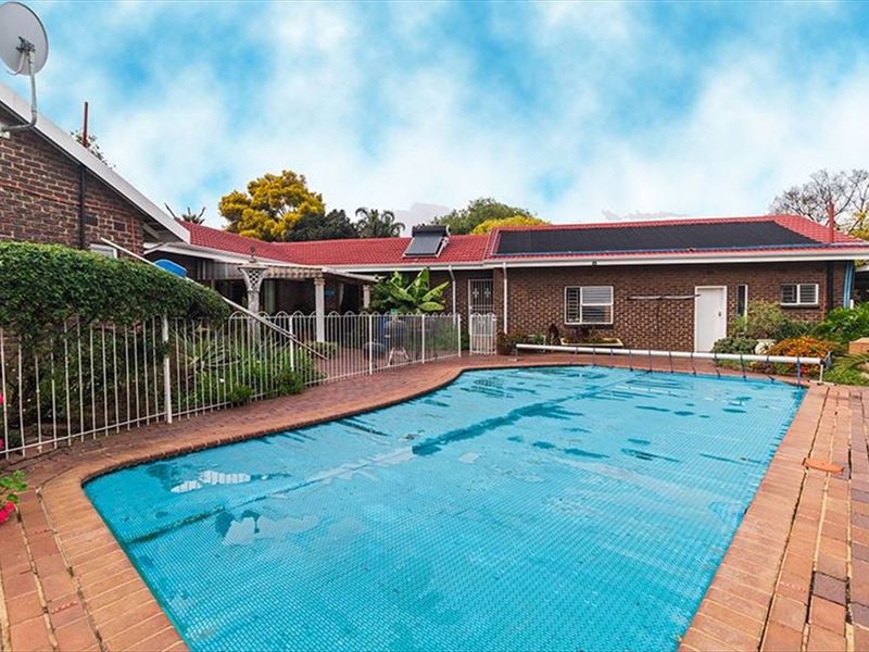 Outdoor pool area featuring a swimming pool with a cover, surrounded by brick paving and enclosed by metal security fencing against a brick house.
