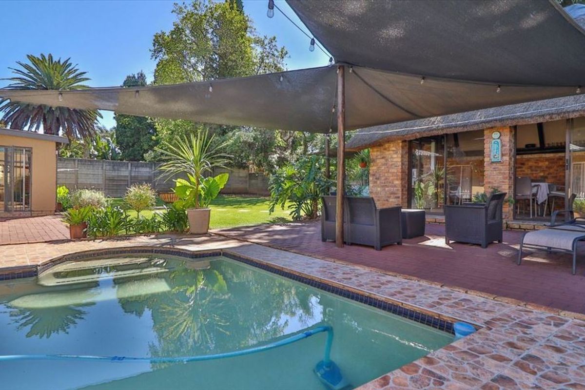 Outdoor pool area featuring a swimming pool, brick paving, and a covered patio with a shade sail and thatched roof structure.