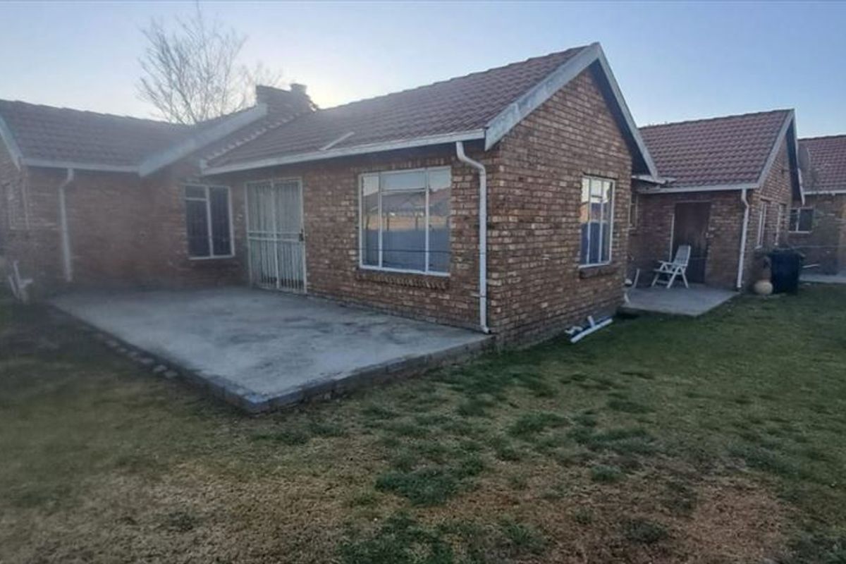 Rear view of a brick house featuring a concrete patio area and a spacious backyard with perimeter walling.