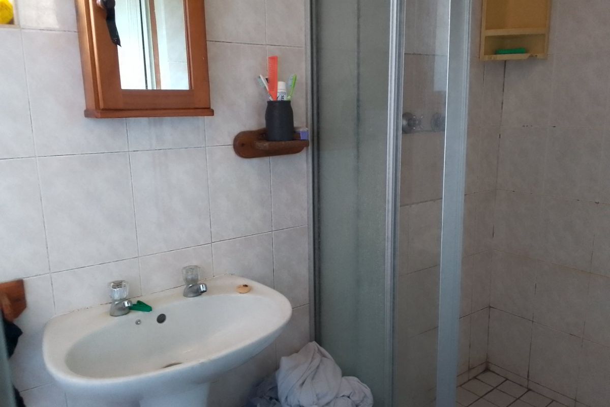 A functional bathroom featuring a pedestal basin, a glass-enclosed shower, and tiled finishes, offering potential for a modern renovation.