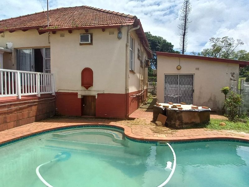 Rear exterior view of the property featuring a swimming pool, raised deck area, and detached outbuilding with a tiled roof.