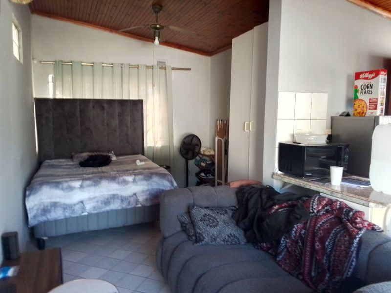 Open-plan living and sleeping area featuring a timber ceiling, ceiling fan, tiled flooring, and built-in storage cupboards.