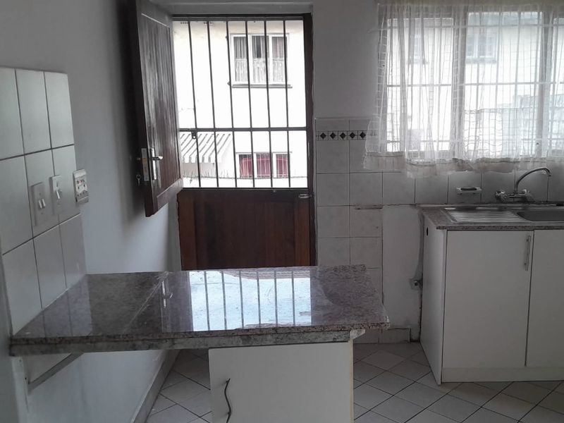 A functional kitchen featuring granite countertops, built-in cabinetry, a stainless steel sink, and tiled flooring, with direct access to an exterior security gate.