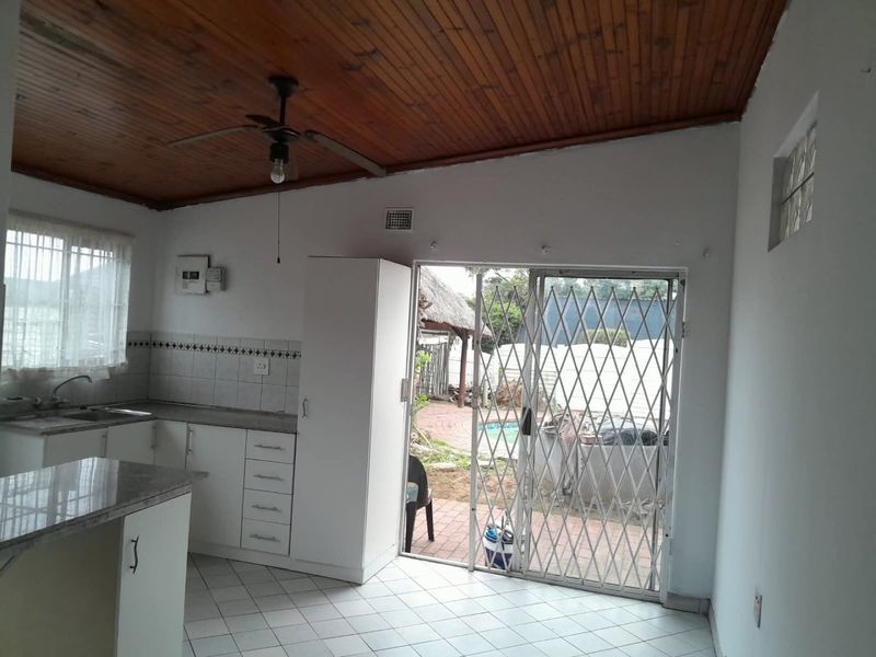 Open plan kitchen area featuring timber ceilings, tiled flooring, and direct access to the outdoor patio through a sliding glass door with security gate.