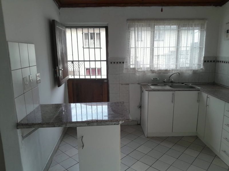 A functional kitchen featuring granite countertops, tiled backsplash, and white cabinetry, with direct access to an exterior door with security gate.
