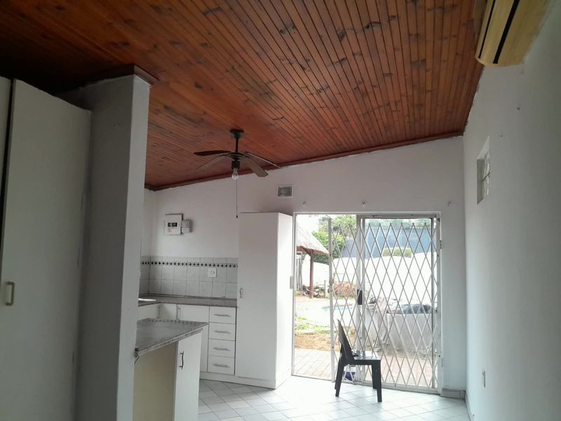 Open plan kitchen and living area featuring a timber ceiling, tiled floors, and direct access to the outdoor patio through a security sliding door.