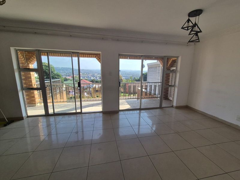 Spacious living area featuring neutral tiled flooring, modern pendant lighting, and dual sliding glass doors opening to a balcony with scenic views.