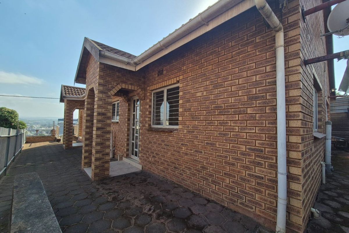 Rear exterior view of a face brick house featuring a paved patio area, security bars on windows, and functional guttering system.