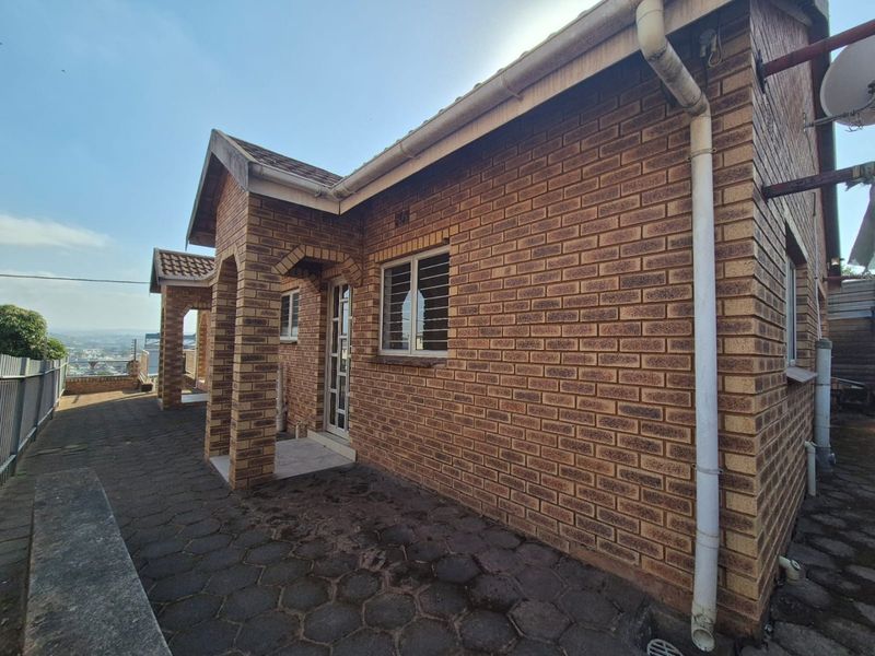 Rear exterior view of a face brick house featuring a paved patio area, security bars on windows, and functional guttering system.