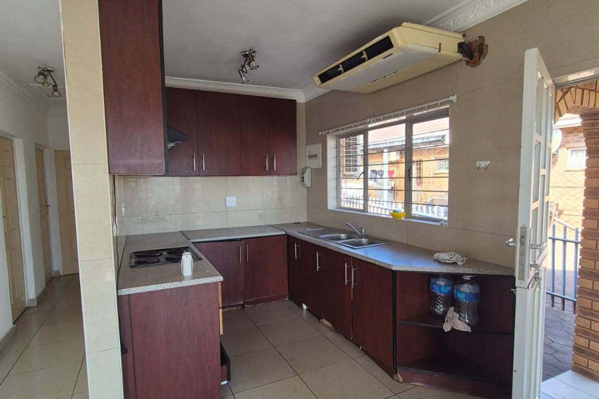 A functional kitchen featuring dark wood cabinetry, laminate countertops, a built-in hob, and tiled flooring, offering a practical layout with direct outdoor access.