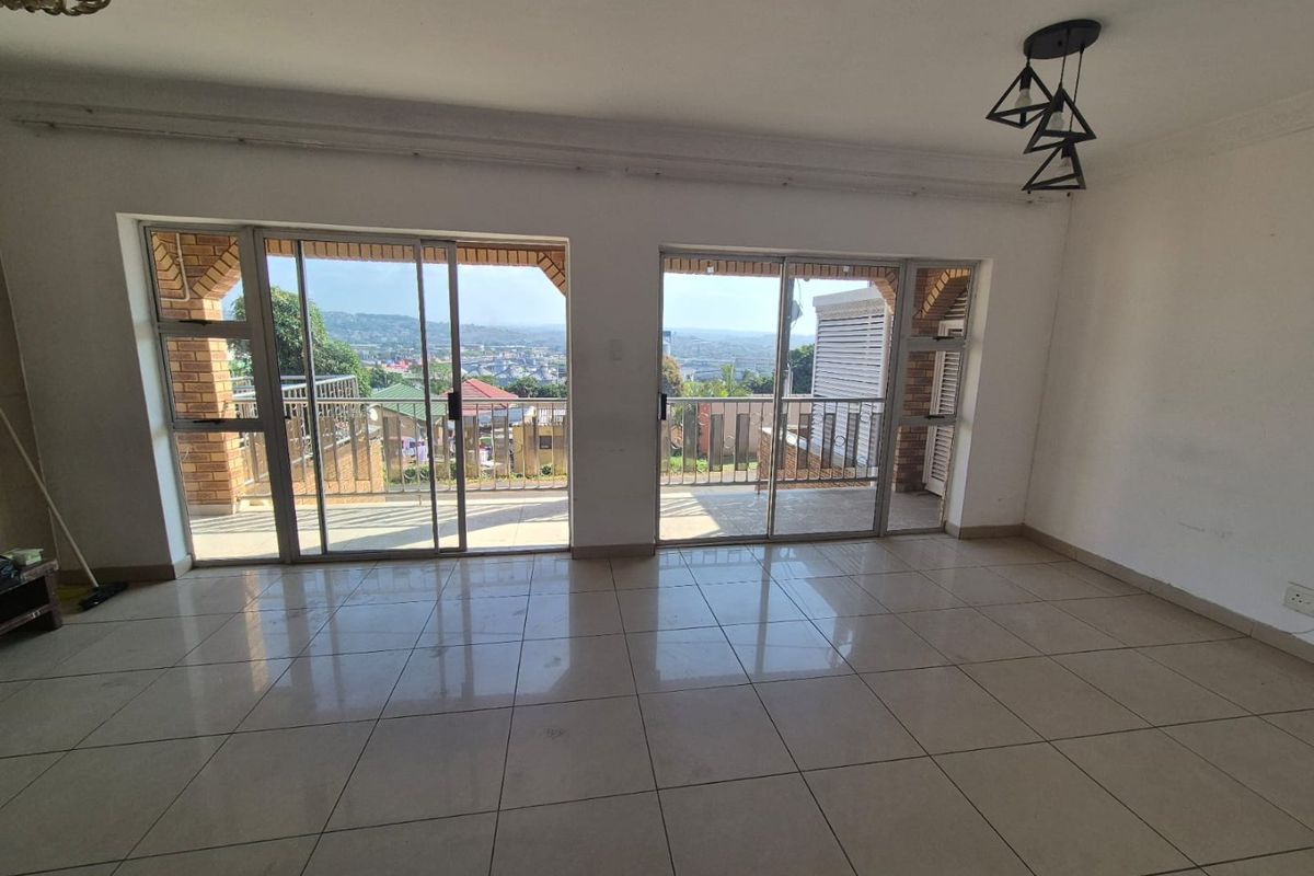Spacious, empty living area featuring large sliding glass doors that open onto a balcony with scenic views and neutral tiled flooring throughout.