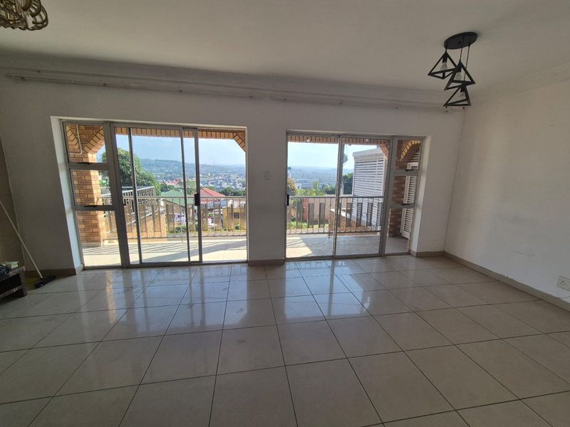Spacious, empty living area featuring large sliding glass doors that open onto a balcony with scenic views and neutral tiled flooring throughout.