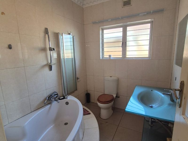 A functional bathroom featuring a built-in bathtub, wall-mounted shower, toilet, and a glass-top basin with tiled finishes throughout.