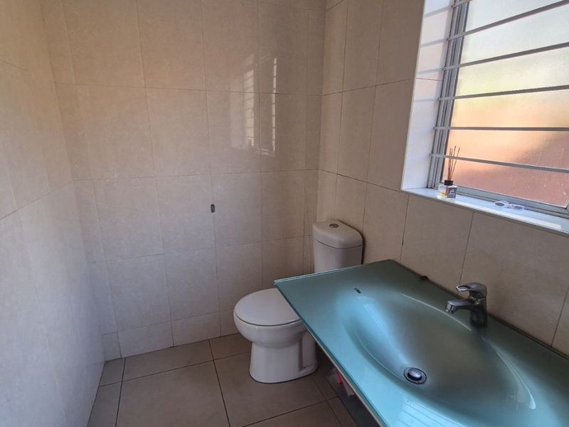 A functional bathroom featuring a glass vanity basin, toilet, and neutral wall and floor tiling with a window for natural light.