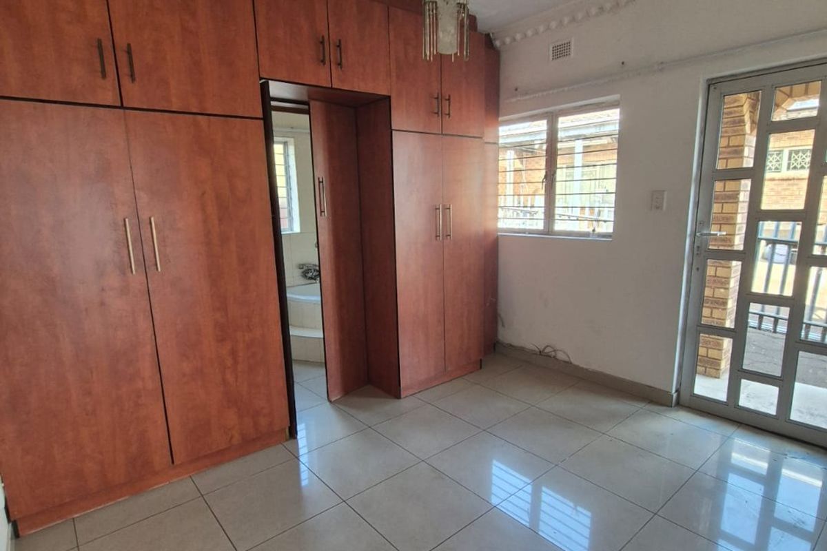 An empty bedroom featuring extensive built-in wooden cupboards, tiled flooring, and direct access to an exterior area through a security gate.