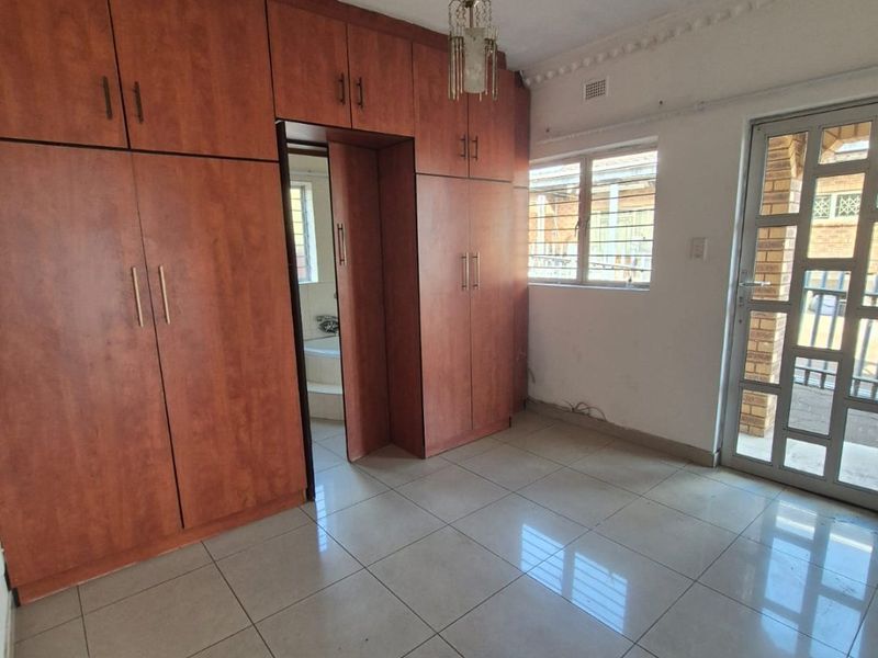 An empty bedroom featuring extensive built-in wooden cupboards, tiled flooring, and direct access to an exterior area through a security gate.