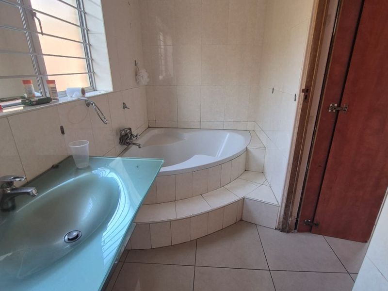 A functional bathroom featuring a corner bathtub, tiled finishes, and a glass vanity countertop with a basin.