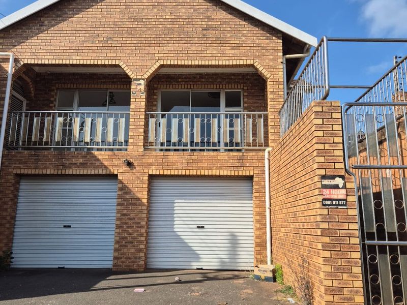 Front elevation of a double-story brick house featuring a double garage with roller shutter doors and an upper-level balcony with metal railings.