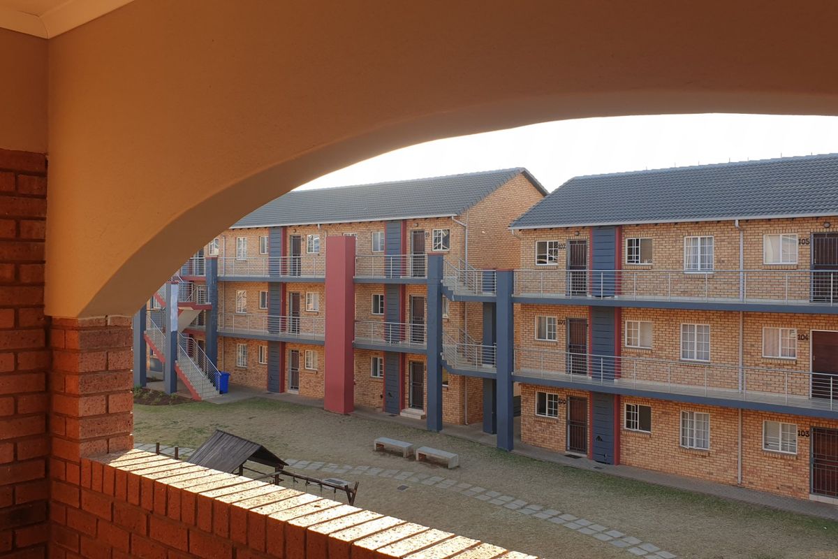 View of the apartment complex exterior featuring brick facade, external staircases, and a shared courtyard area.