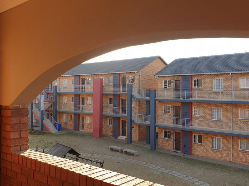 View of the apartment complex exterior featuring brick facade, external staircases, and a shared courtyard area.