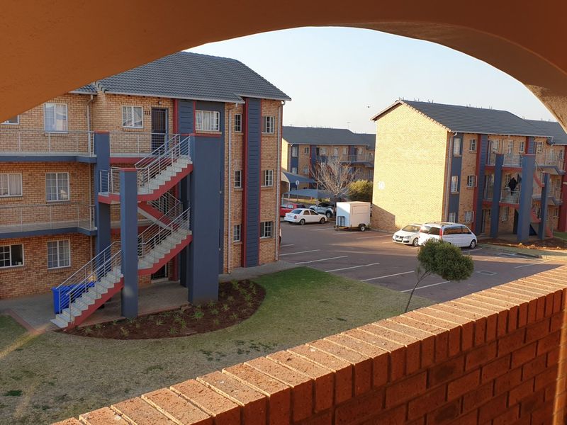 View of the apartment complex exterior featuring brick facades, external staircases, and a communal parking area with landscaped grounds.