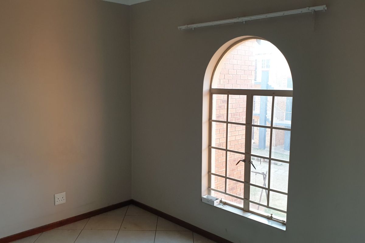 An empty bedroom featuring neutral walls, tiled flooring, and a distinctive arched window with a curtain rail installed.