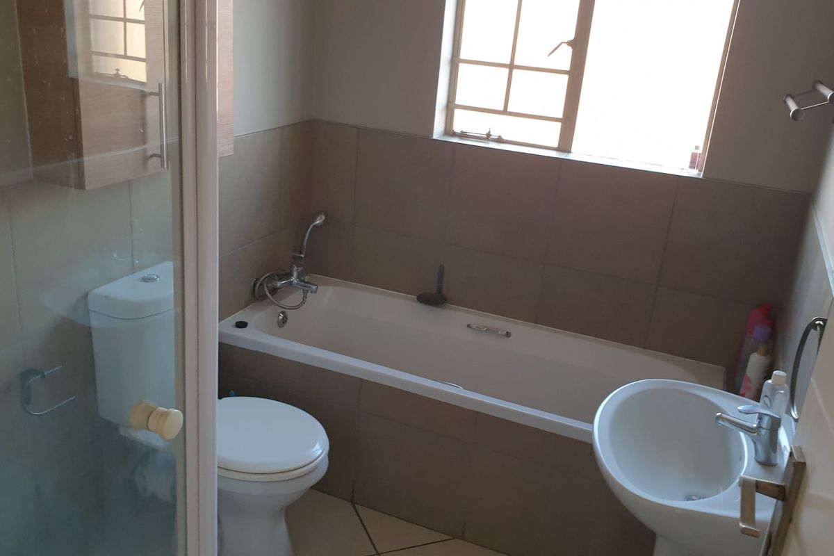 A functional bathroom featuring a bathtub, separate shower enclosure, pedestal basin, and tiled finishes, offering a practical layout for an apartment.