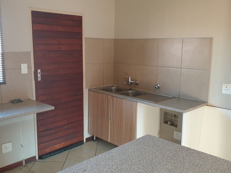 A functional kitchen area featuring laminate countertops, a double sink, tiled splashbacks, and tiled flooring, currently vacant and ready for updates.