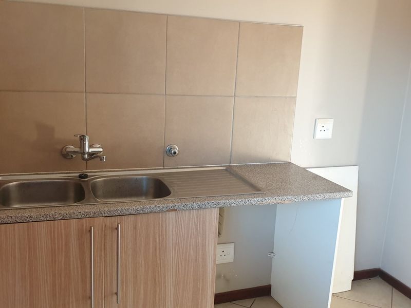 A compact kitchen area featuring a double bowl sink, laminate cabinetry, and tiled splashback, currently requiring minor repairs to the cabinetry and plumbing fixtures.