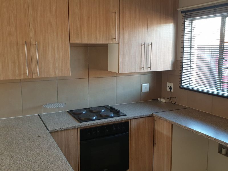 A functional kitchen featuring light wood-finish cabinetry, granite-look laminate countertops, a built-in electric oven and hob, and neutral tiled splashbacks.