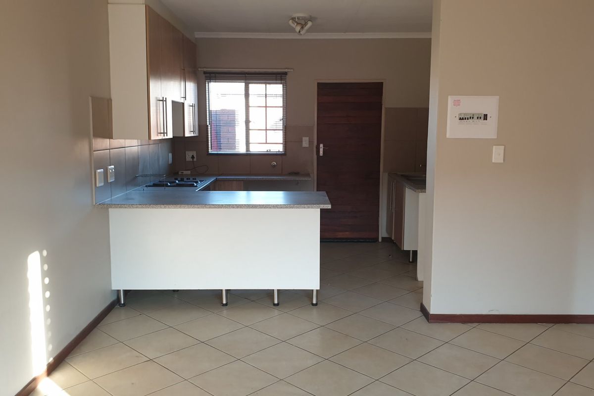 A functional kitchen featuring built-in cabinetry, laminate countertops, a hob, and tiled flooring, presented in a clean, empty space ready for personalization.