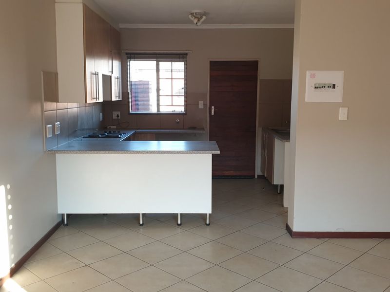 A functional kitchen featuring built-in cabinetry, laminate countertops, a hob, and tiled flooring, presented in a clean, empty space ready for personalization.