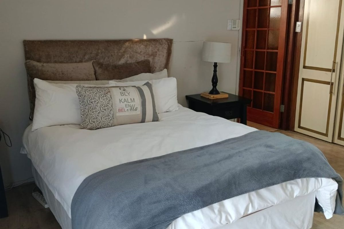 A bedroom featuring laminate flooring, a built-in wardrobe, and a classic timber-framed glass door leading to the hallway.