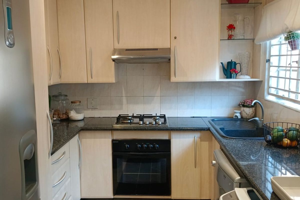 Compact kitchen featuring light wood cabinetry, granite countertops, gas hob, built-in oven, and tiled flooring with a functional layout.