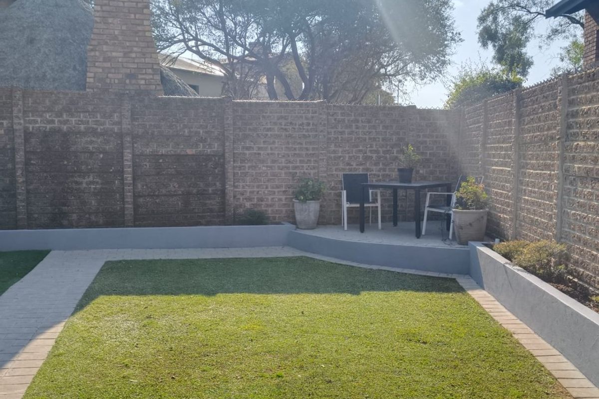A private rear garden featuring a paved patio area, raised garden beds, and a well-maintained lawn enclosed by brick boundary walls.