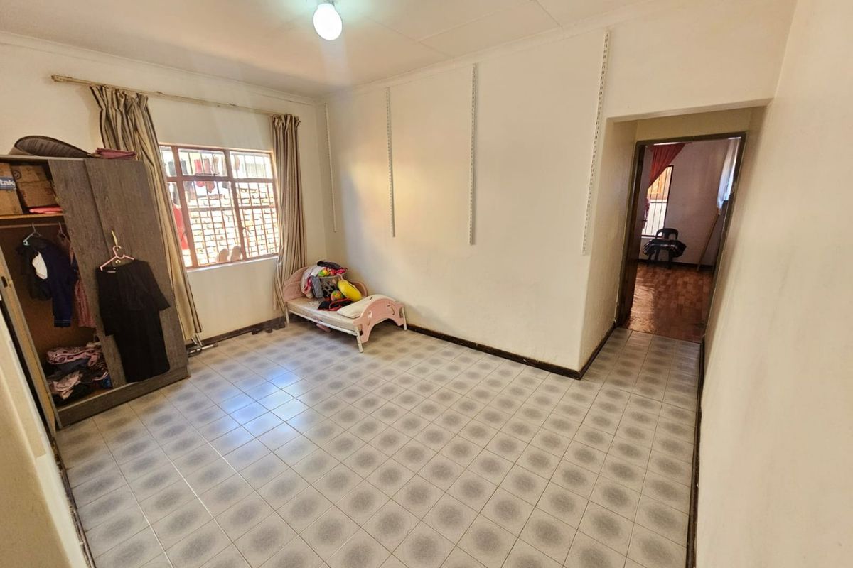 A bedroom featuring tiled flooring, security bars on the window, and wall-mounted shelving tracks, offering a functional space with potential for cosmetic updates.