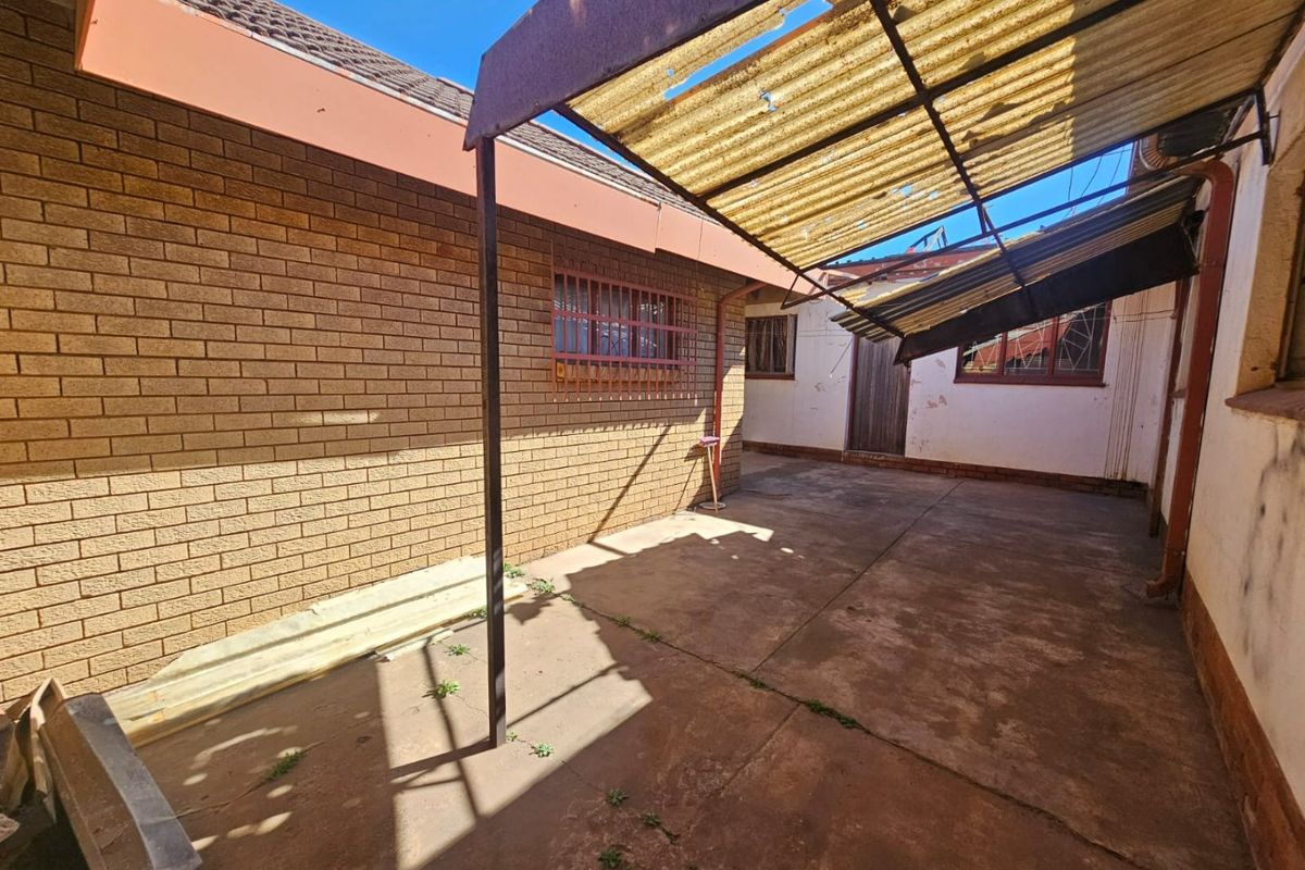 Rear exterior area featuring brick walls, concrete paving, and a damaged corrugated roof structure requiring maintenance and repair.