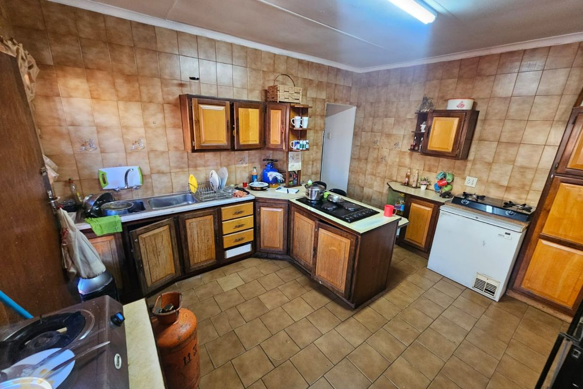 A functional kitchen featuring extensive wooden cabinetry, tiled walls and flooring, and integrated cooking hobs, offering a dated aesthetic ready for modernization.