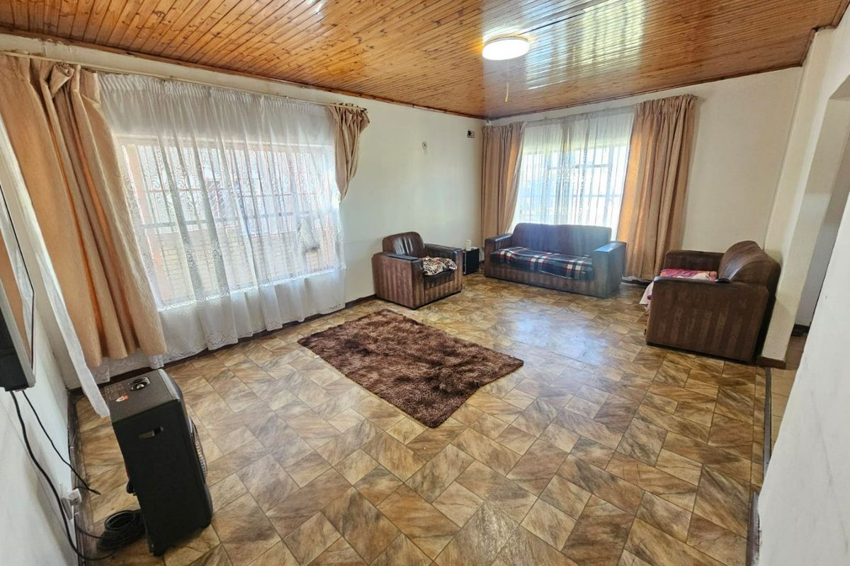 A living room featuring a timber-clad ceiling and tiled flooring, offering a dated aesthetic that could be modernized with contemporary finishes.